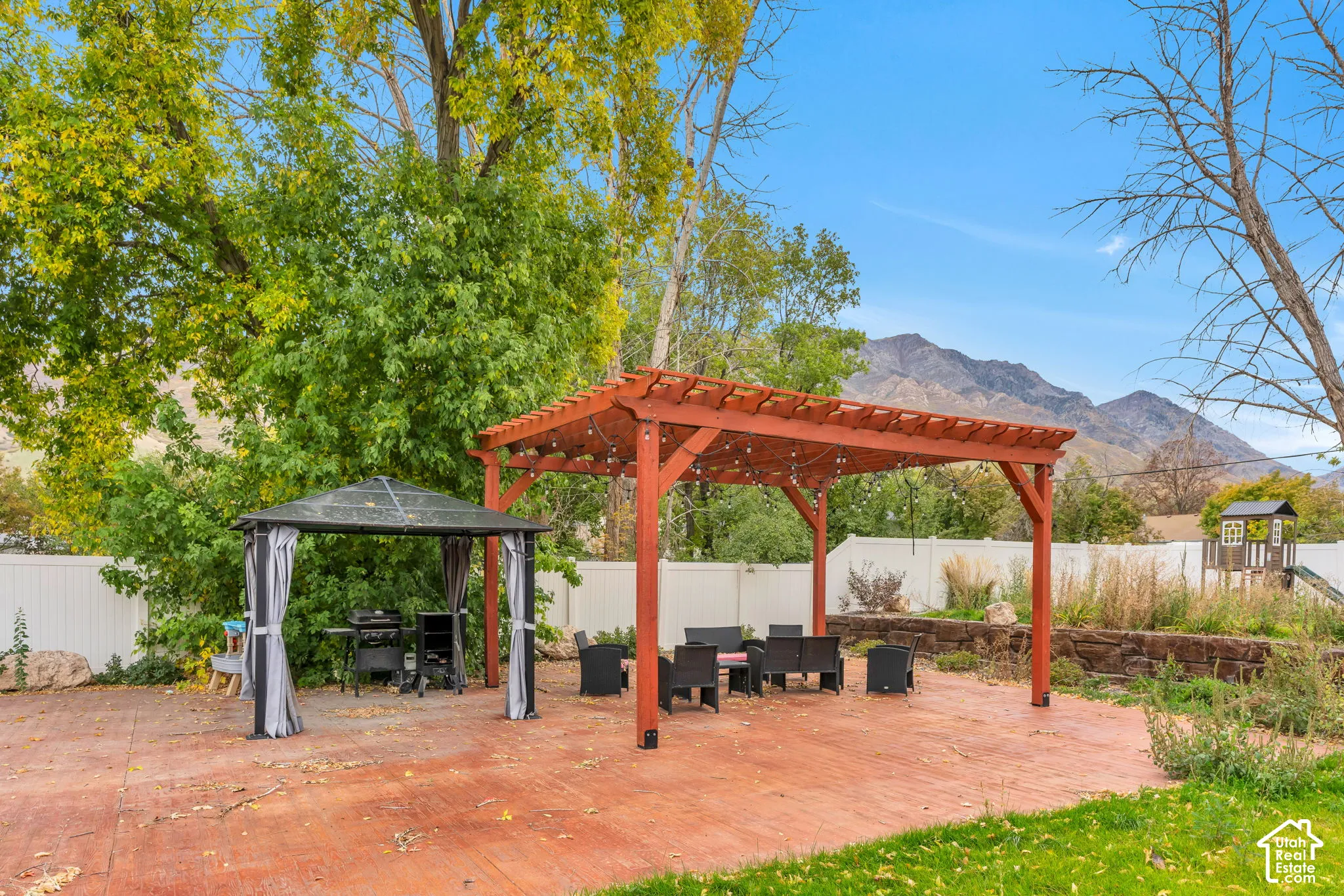 Stamped concrete patio featuring a wood pergola, a metal-frame gazebo, a stone retaining wall, and mountain backdrop