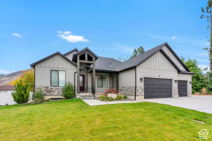 Contemporary residence featuring multi-material siding, stacked stone veneer accents, a covered entryway with structural timber framing, a three-car garage, and mountain-range backdrop