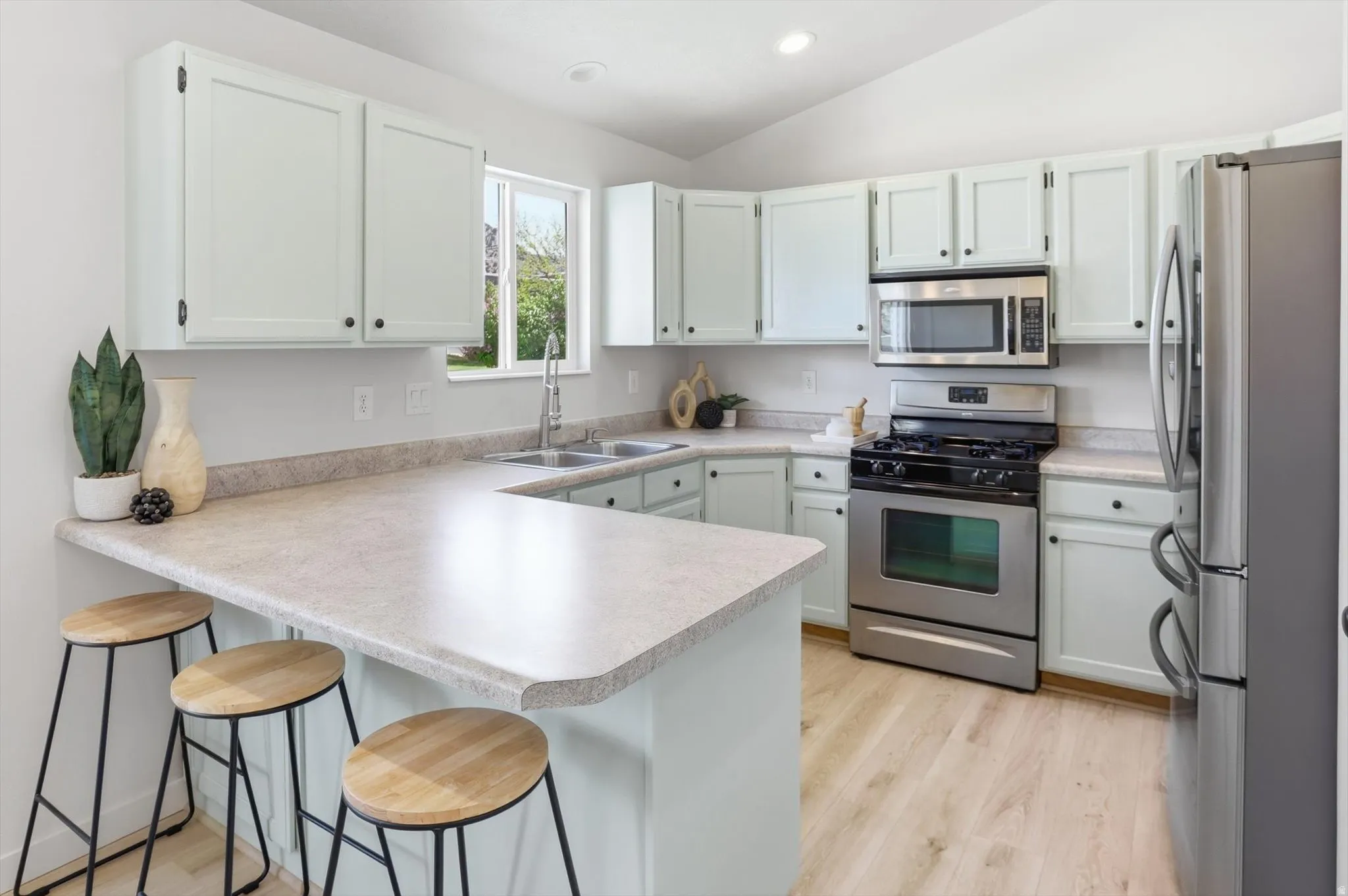 Kitchen featuring a kitchen breakfast bar, stainless steel appliances, a peninsula, light wood finished floors, and vaulted ceiling