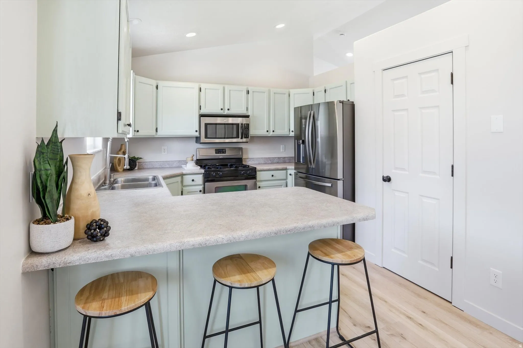 Kitchen with breakfast bar, stainless steel appliances, light countertops, a peninsula, and lofted ceiling
