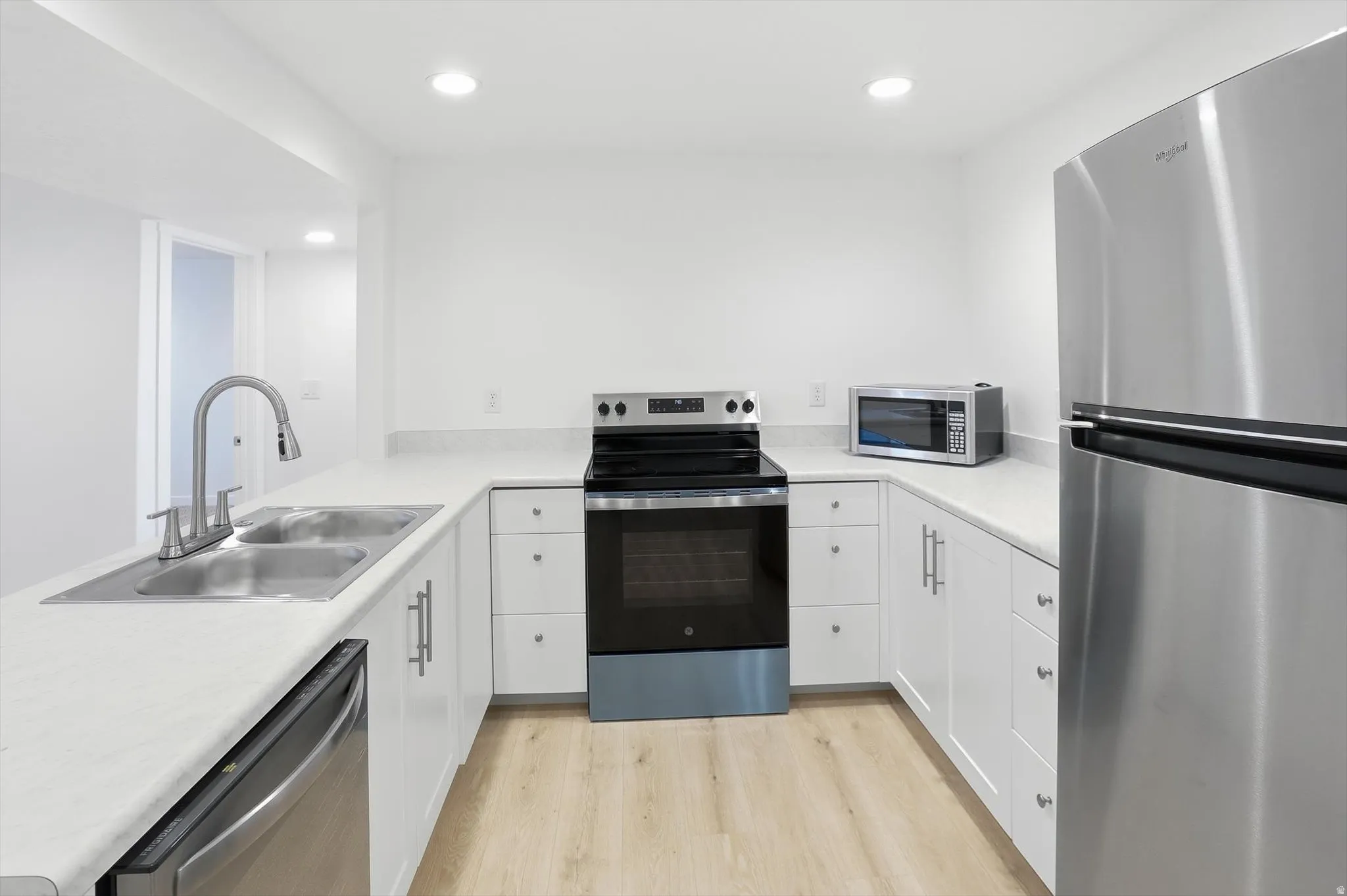 Basement kitchen with stainless steel appliances, light countertops, recessed lighting, a peninsula, and white cabinetry