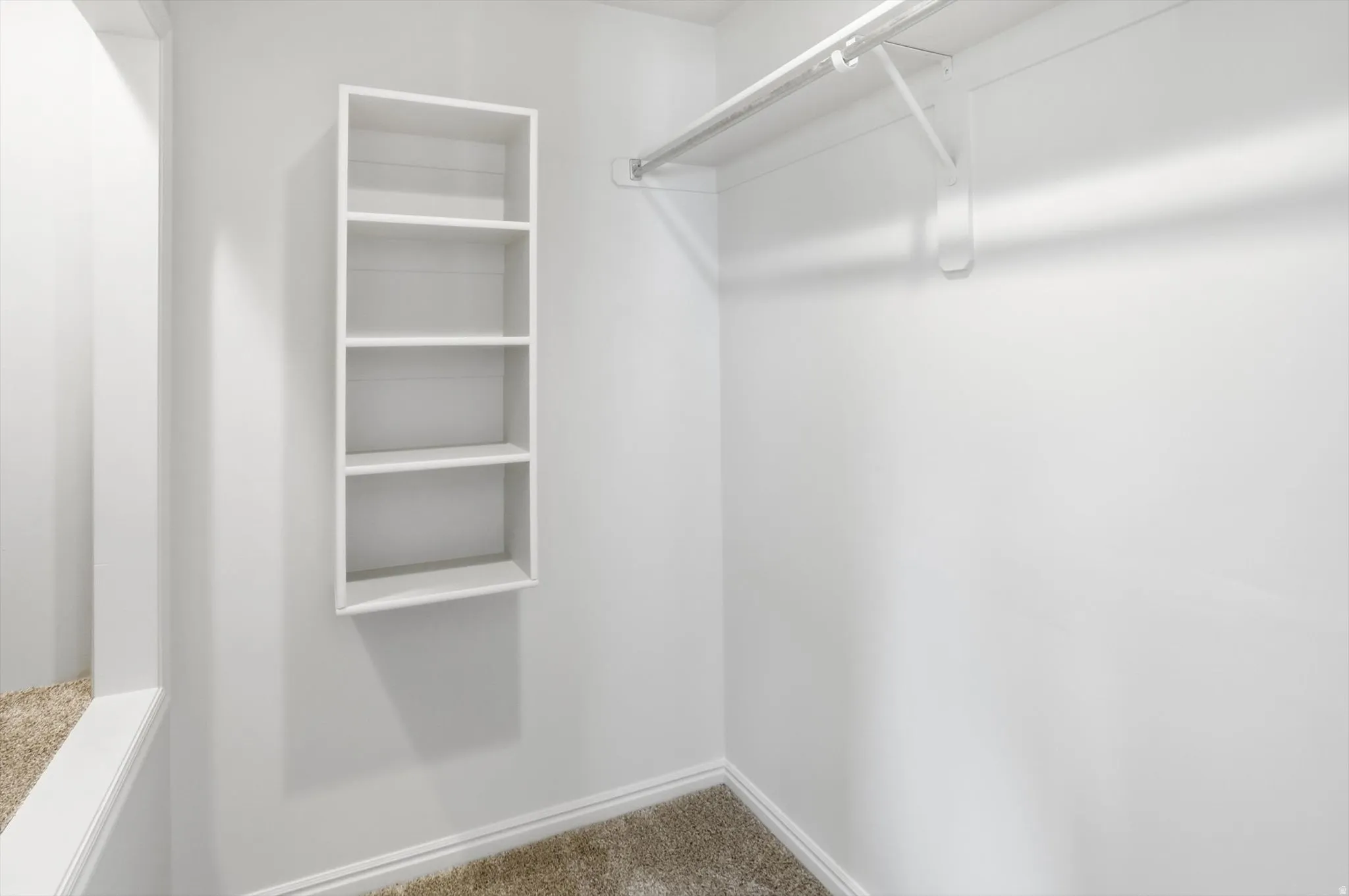 Walk in closet in the primary ensuite with light colored carpet
