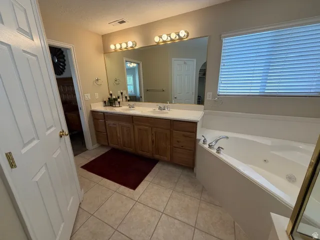 Full bath with light tile patterned floors, double vanity, a jetted tub, and a textured ceiling