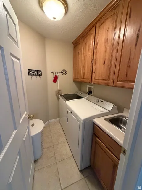 Laundry room with cabinet space, washer and clothes dryer, light tile patterned floors, and a textured ceiling