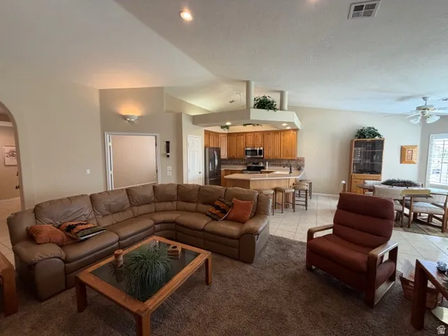Living room with arched walkways, ceiling fan, light tile patterned floors, and vaulted ceiling