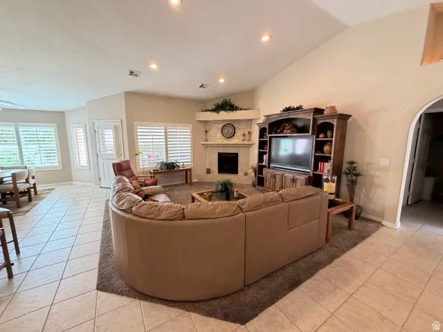 Living room featuring arched walkways, light tile patterned flooring, lofted ceiling, a fireplace, and plenty of natural light