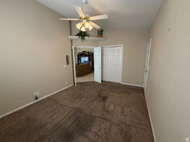 Empty room featuring ceiling fan, vaulted ceiling, and dark colored carpet