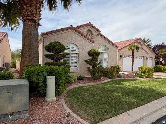 Mediterranean / spanish home with a tile roof, stucco siding, a garage, and a front lawn