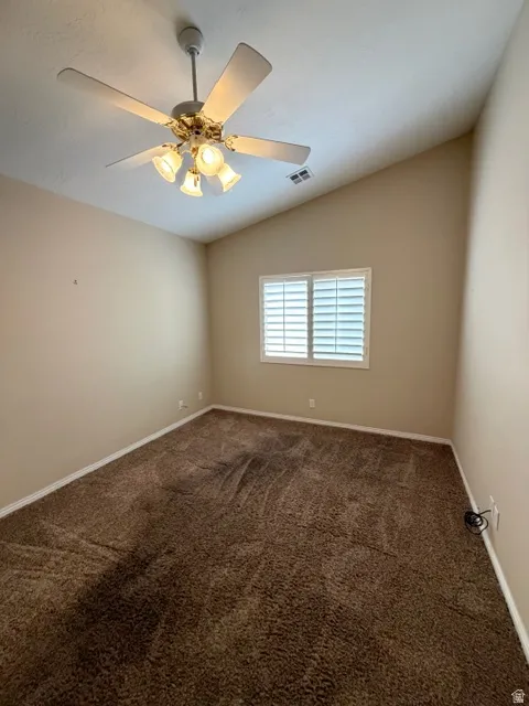 Empty room with lofted ceiling, dark colored carpet, and a ceiling fan