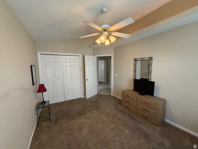 Unfurnished bedroom with dark colored carpet, a closet, ceiling fan, and lofted ceiling