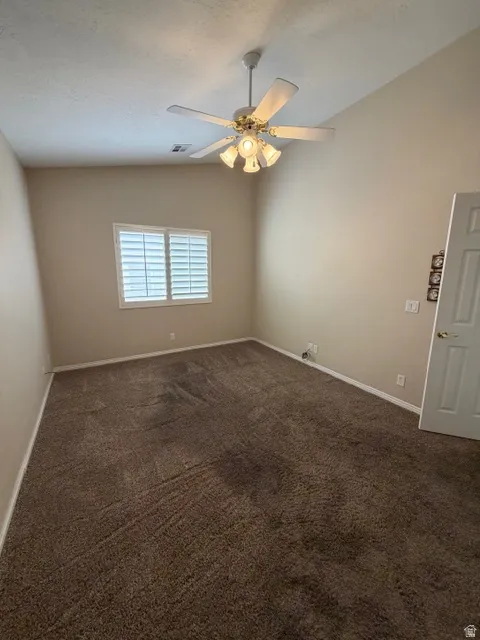 Unfurnished room with vaulted ceiling, dark colored carpet, and ceiling fan