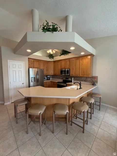 Kitchen featuring a kitchen breakfast bar, wood finish cabinets, stainless steel appliances, light countertops, and a peninsula