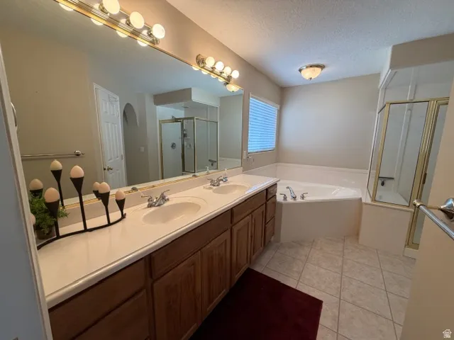 Bathroom with double vanity, a bath, light tile patterned floors, a stall shower, and a textured ceiling