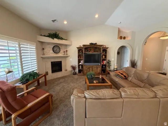 Carpeted living area featuring arched walkways, lofted ceiling, a fireplace, and recessed lighting