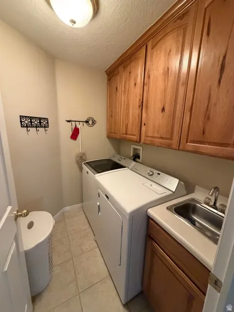 Laundry room with cabinet space, separate washer and dryer, light tile patterned floors, and a textured ceiling