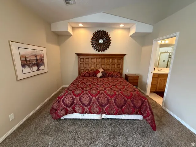 Bedroom featuring ensuite bath, carpet floors, and vaulted ceiling