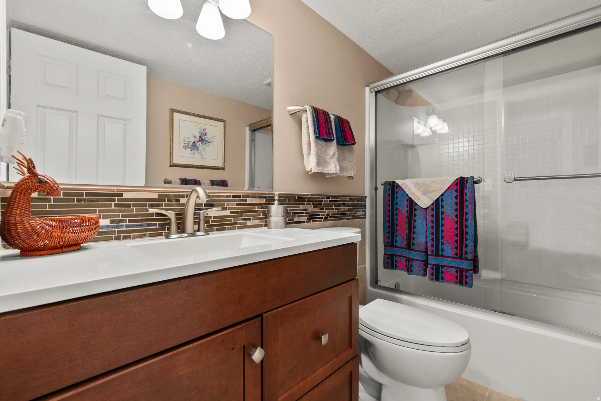 Full bathroom featuring vanity, bath / shower combo with glass door, a textured ceiling, and backsplash