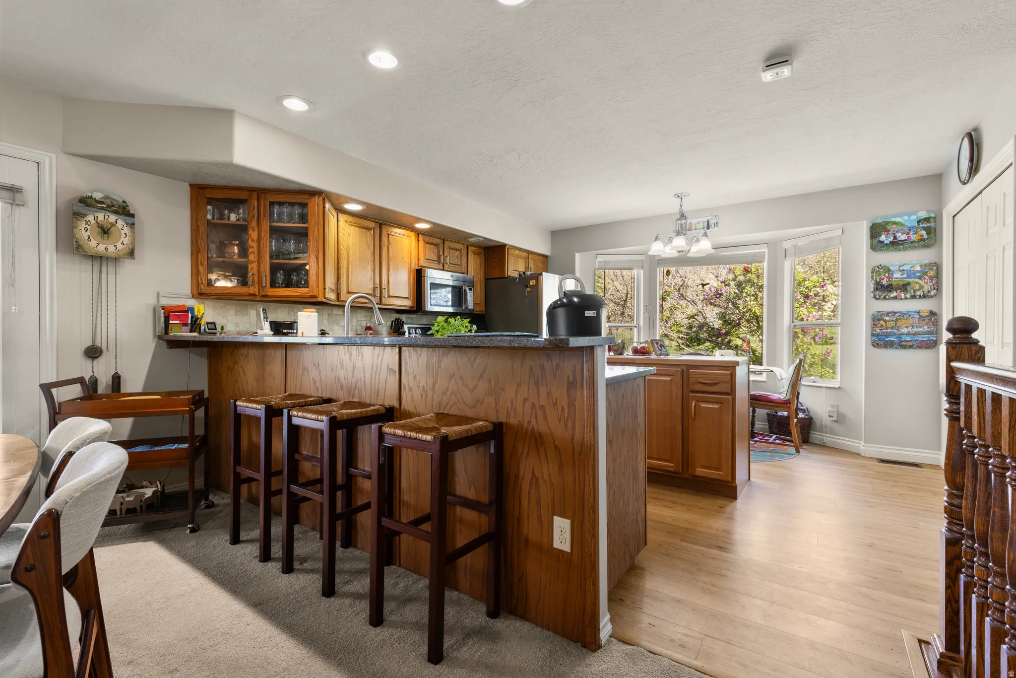 Kitchen with wood finish cabinetry, a peninsula, dark countertops, hanging lights, and glass insert cabinets