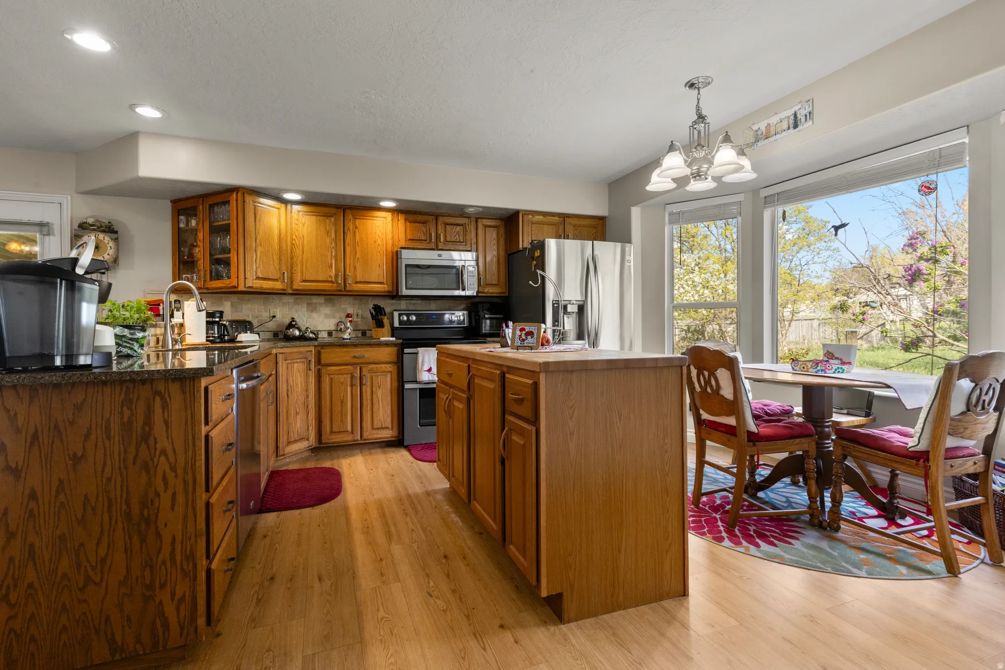 Kitchen with wood finish cabinets, stainless steel appliances, a chandelier, light wood-style floors, and glass fronted cabinets