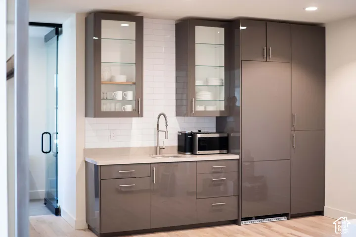 Bar with glass fronted cabinets, modern cabinets, light wood-style floors, and paneled refrigerator