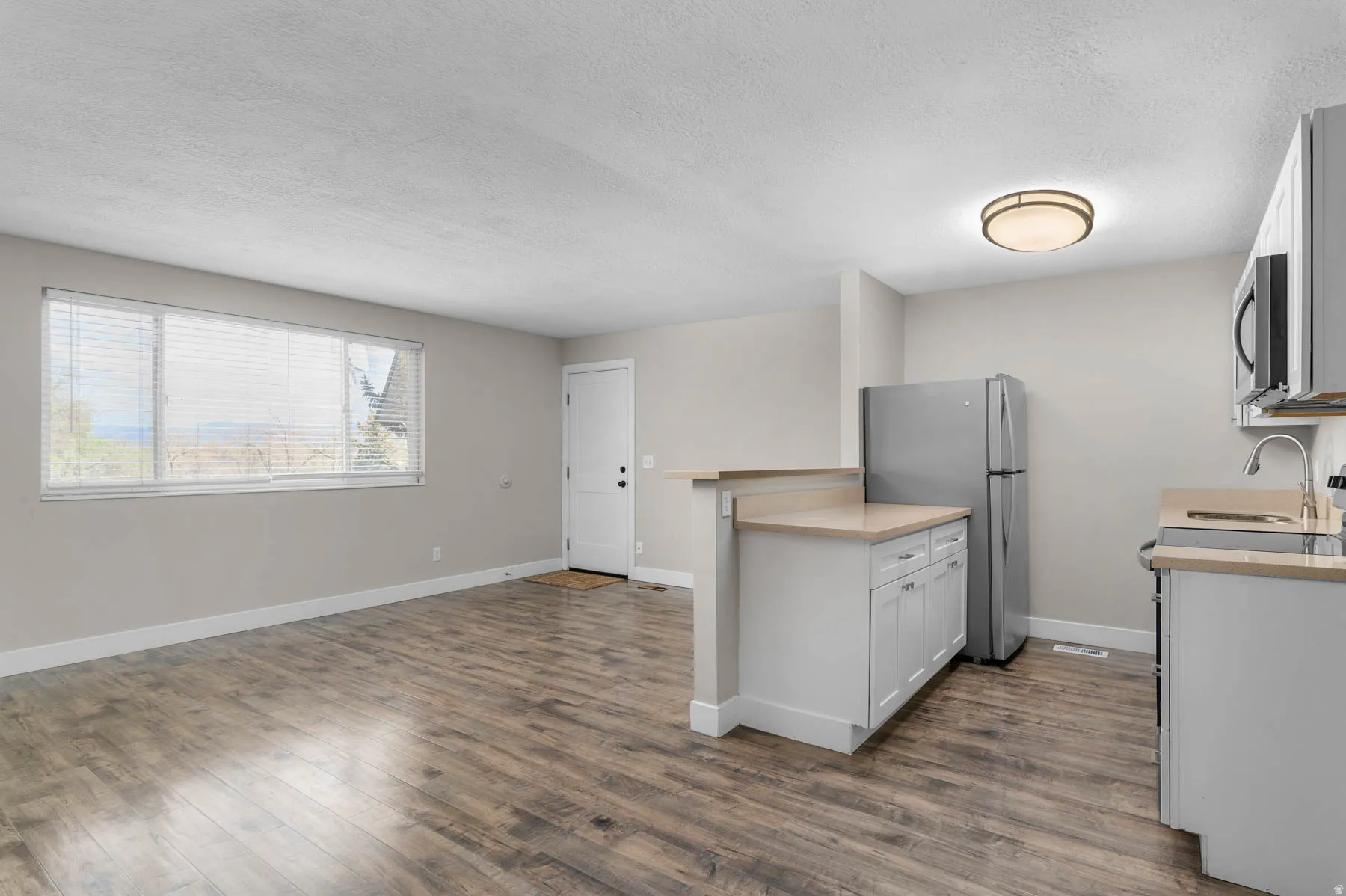 Kitchen featuring light countertops, stainless steel appliances, dark wood-type flooring, open floor plan, and a textured ceiling