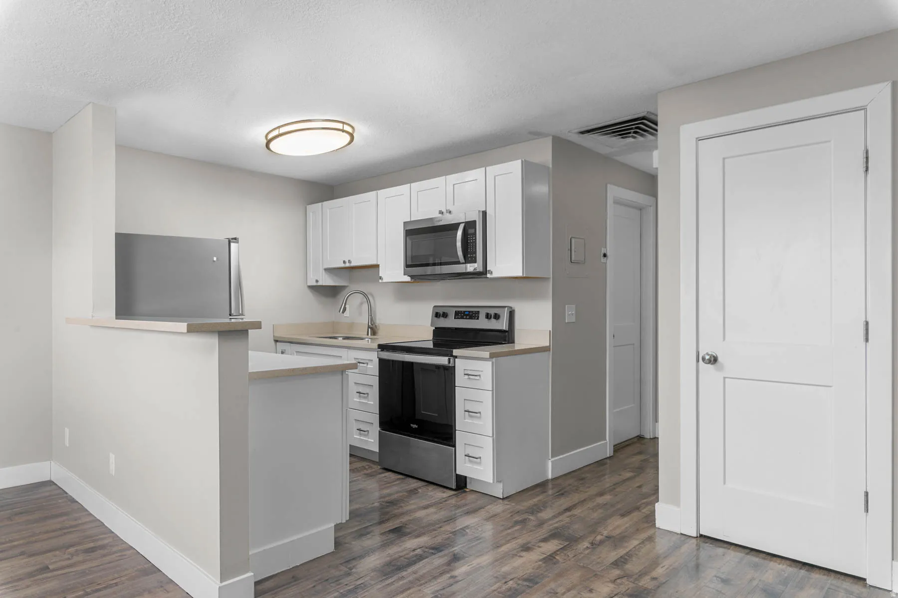Kitchen featuring light countertops, stainless steel appliances, white cabinets, dark wood-style floors, and a peninsula