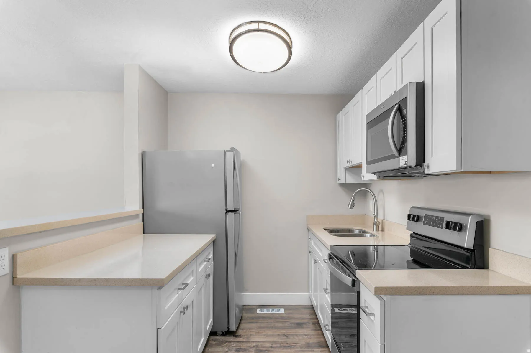 Kitchen featuring stainless steel appliances, white cabinetry, light wood finished floors, a textured ceiling, and light stone countertops
