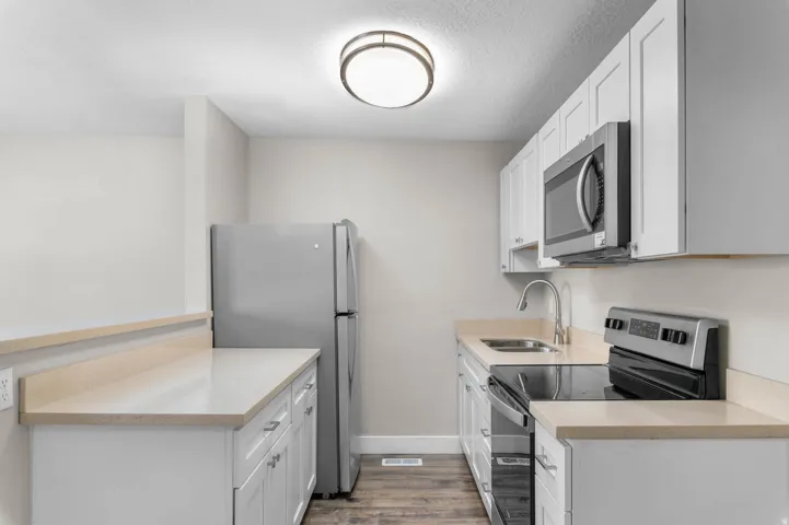 Kitchen featuring stainless steel appliances, white cabinetry, light wood finished floors, a textured ceiling, and light stone countertops