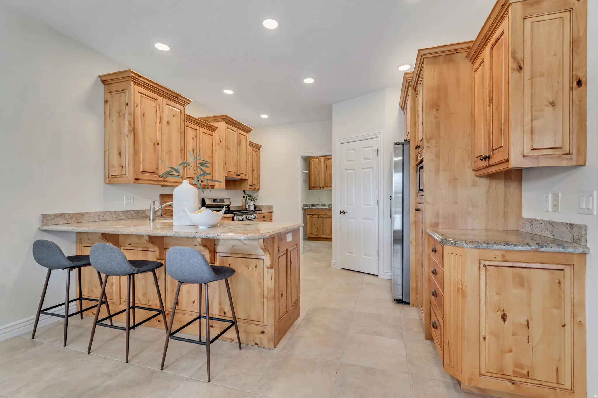 Kitchen with a kitchen breakfast bar, a peninsula, light stone countertops, light wood finish cabinets, and stainless steel appliances