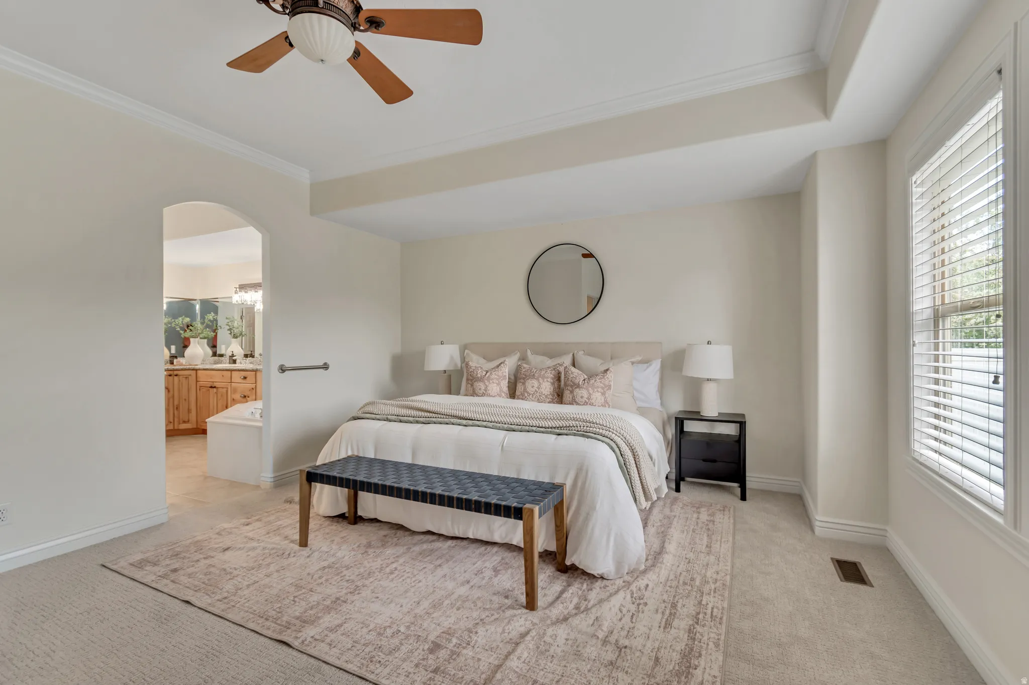 Bedroom with crown molding, light carpet, ceiling fan, ensuite bath, and arched walkways