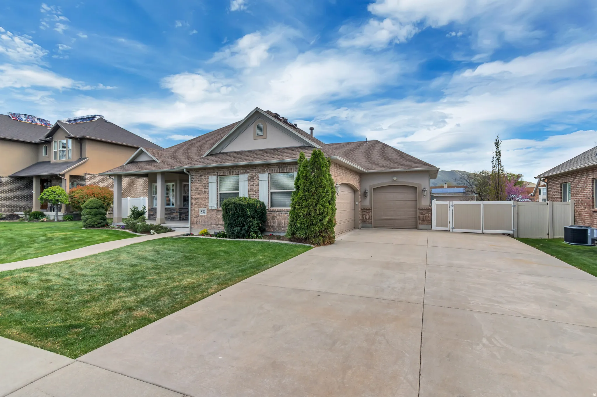 View of front of property featuring a gate, an attached garage, concrete driveway, brick siding, and roof with shingles