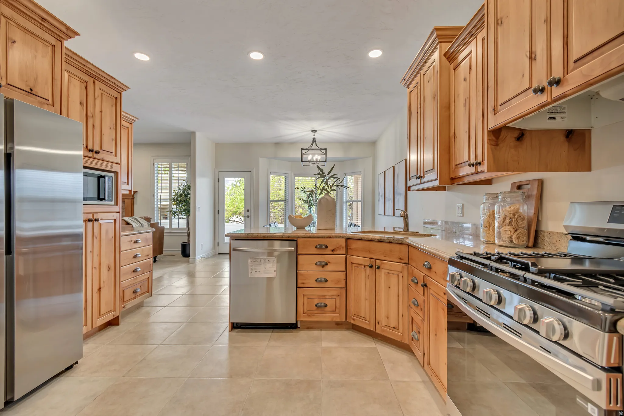 Kitchen with stainless steel appliances, a peninsula, light stone countertops, light tile patterned flooring, and pendant lighting