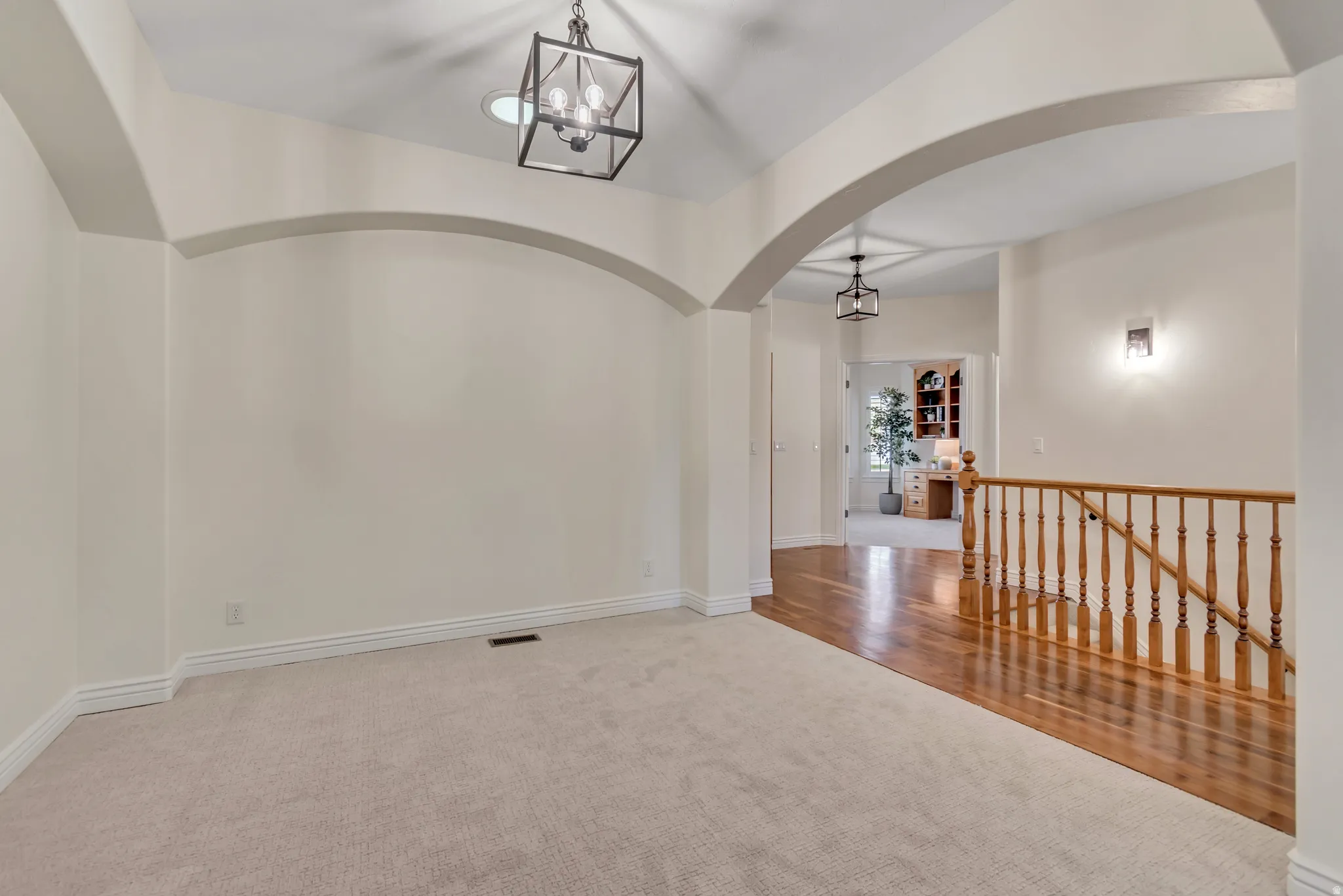 Empty room featuring light colored carpet, arched walkways, and suspended lighting