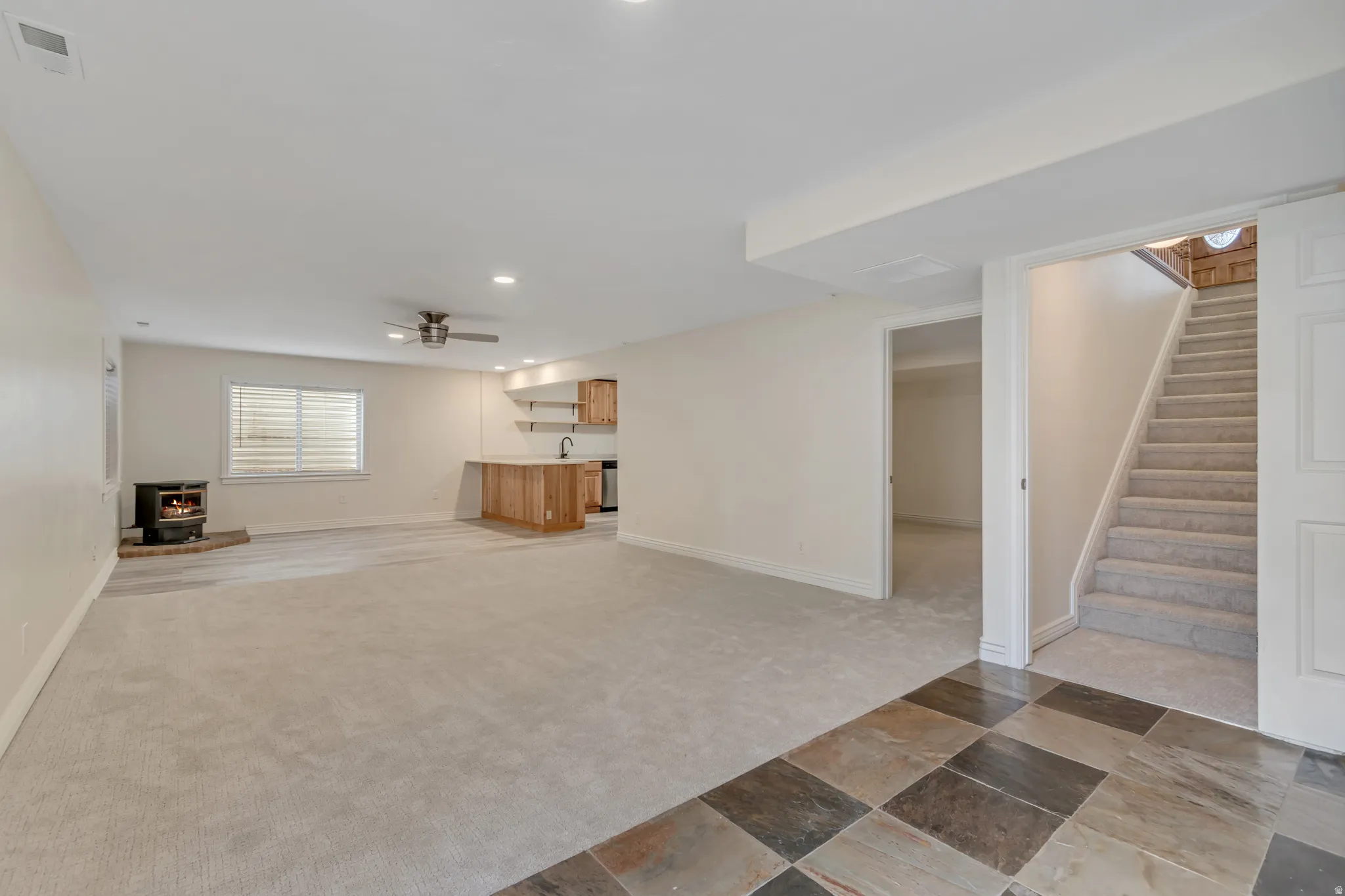 Unfurnished living room featuring light colored carpet, a wood stove, recessed lighting, a ceiling fan, and light stone finish flooring