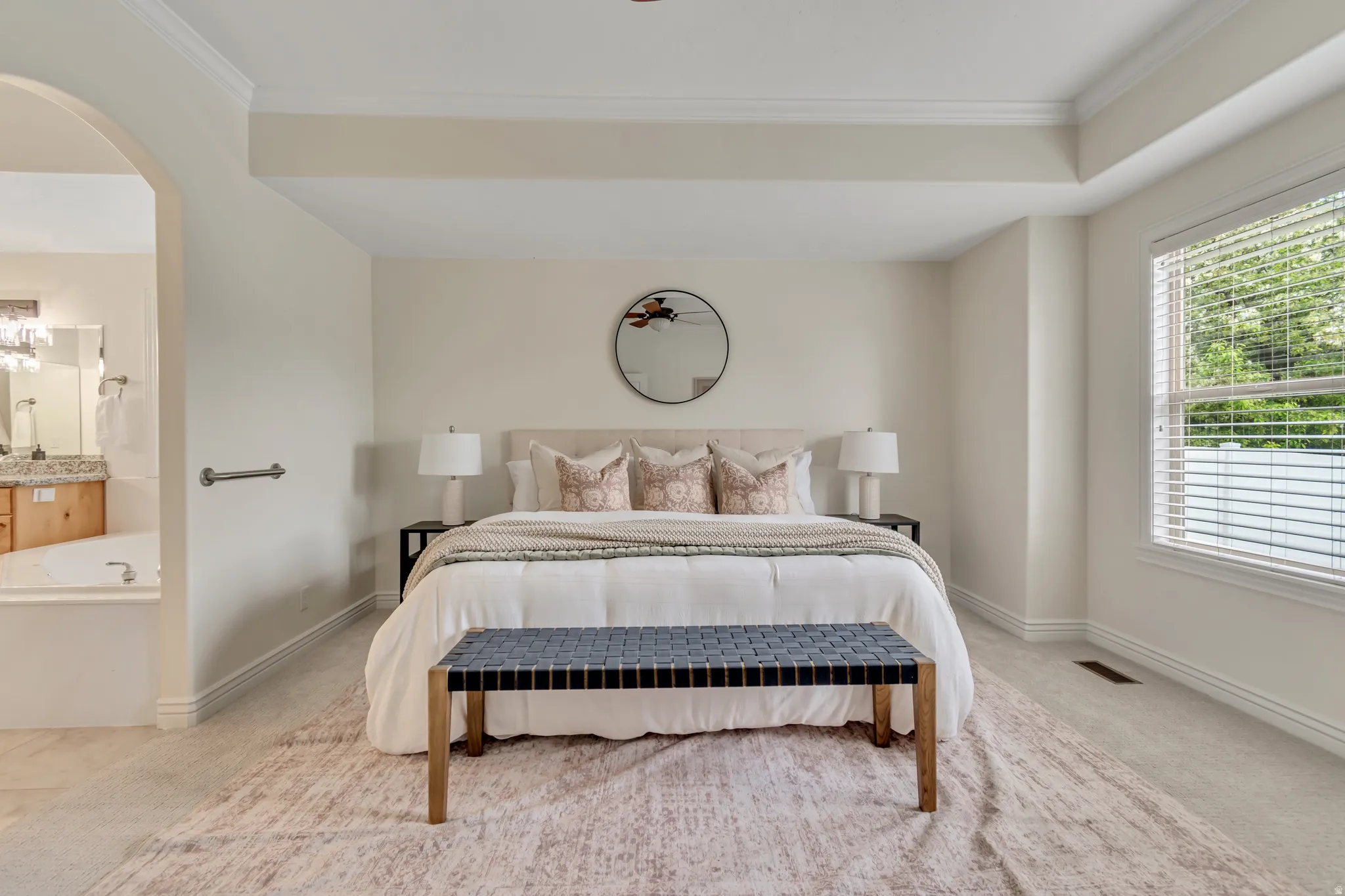 Bedroom featuring light colored carpet, ornamental molding, arched walkways, and ensuite bath