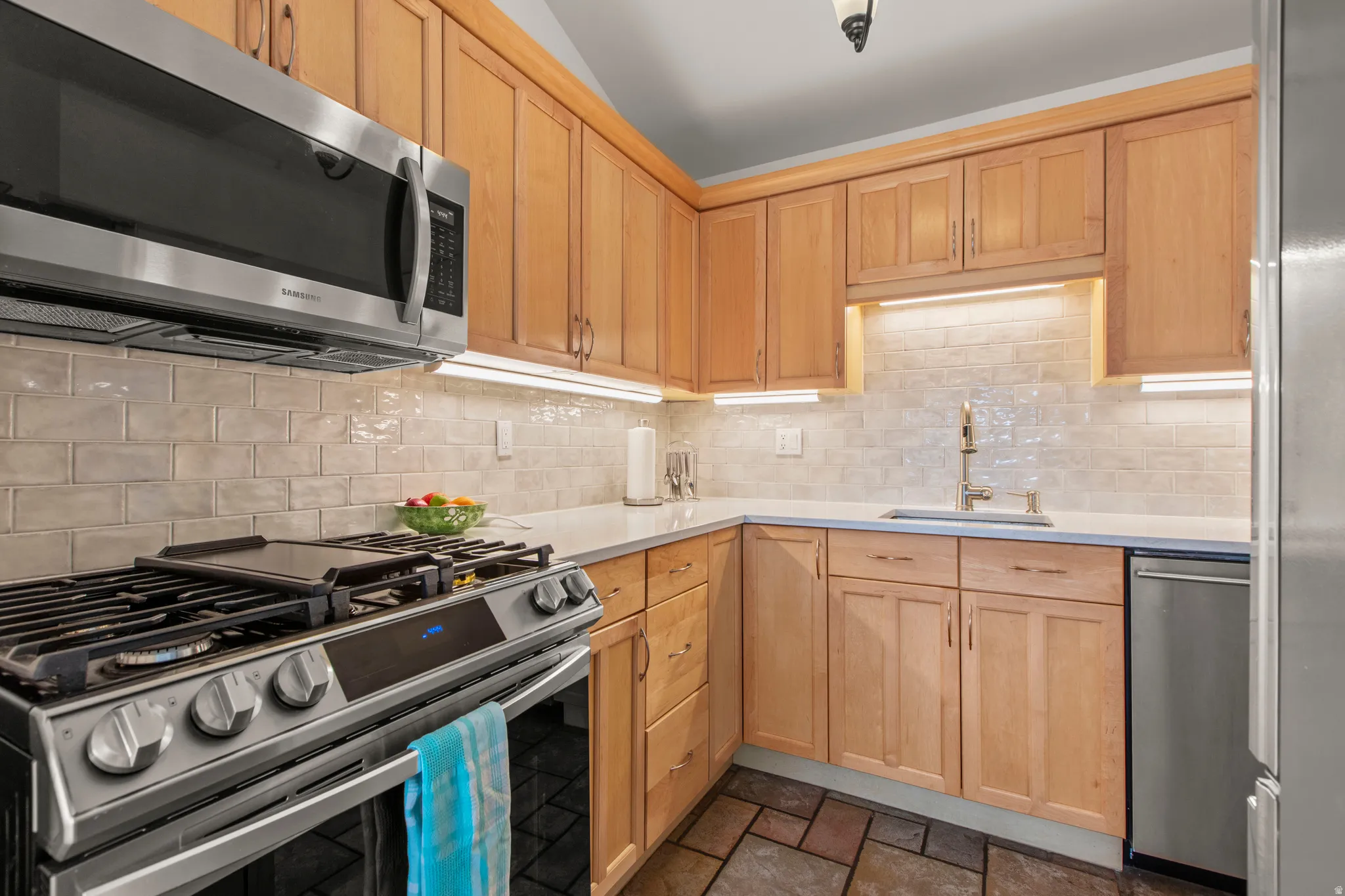 Kitchen featuring light wood finish cabinetry, stainless steel appliances, tile backsplash, and light stone counters