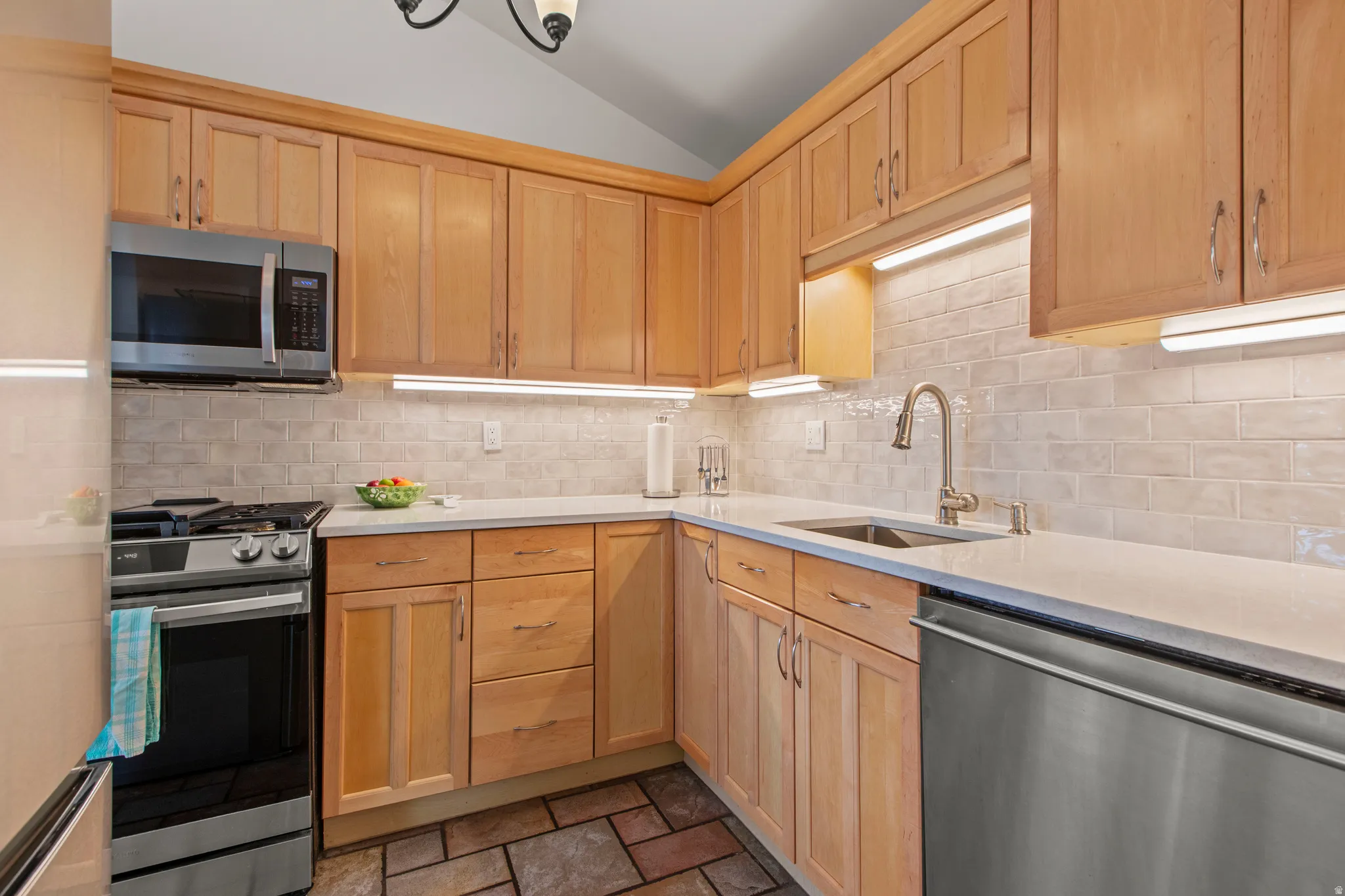 Kitchen featuring light wood finish cabinetry, stainless steel appliances, tile backsplash, and light stone counters