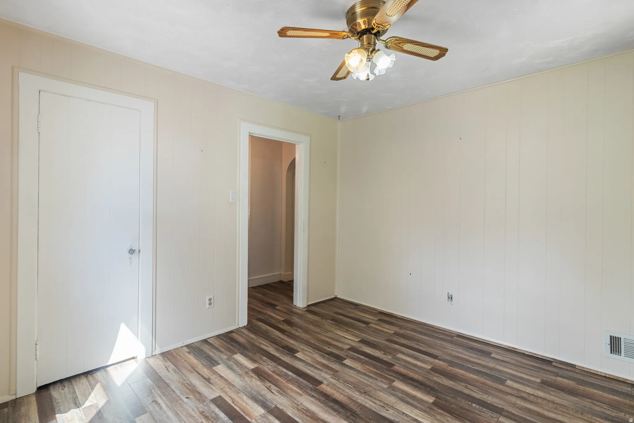 Unfurnished bedroom with dark wood-type flooring, a ceiling fan, and wood walls