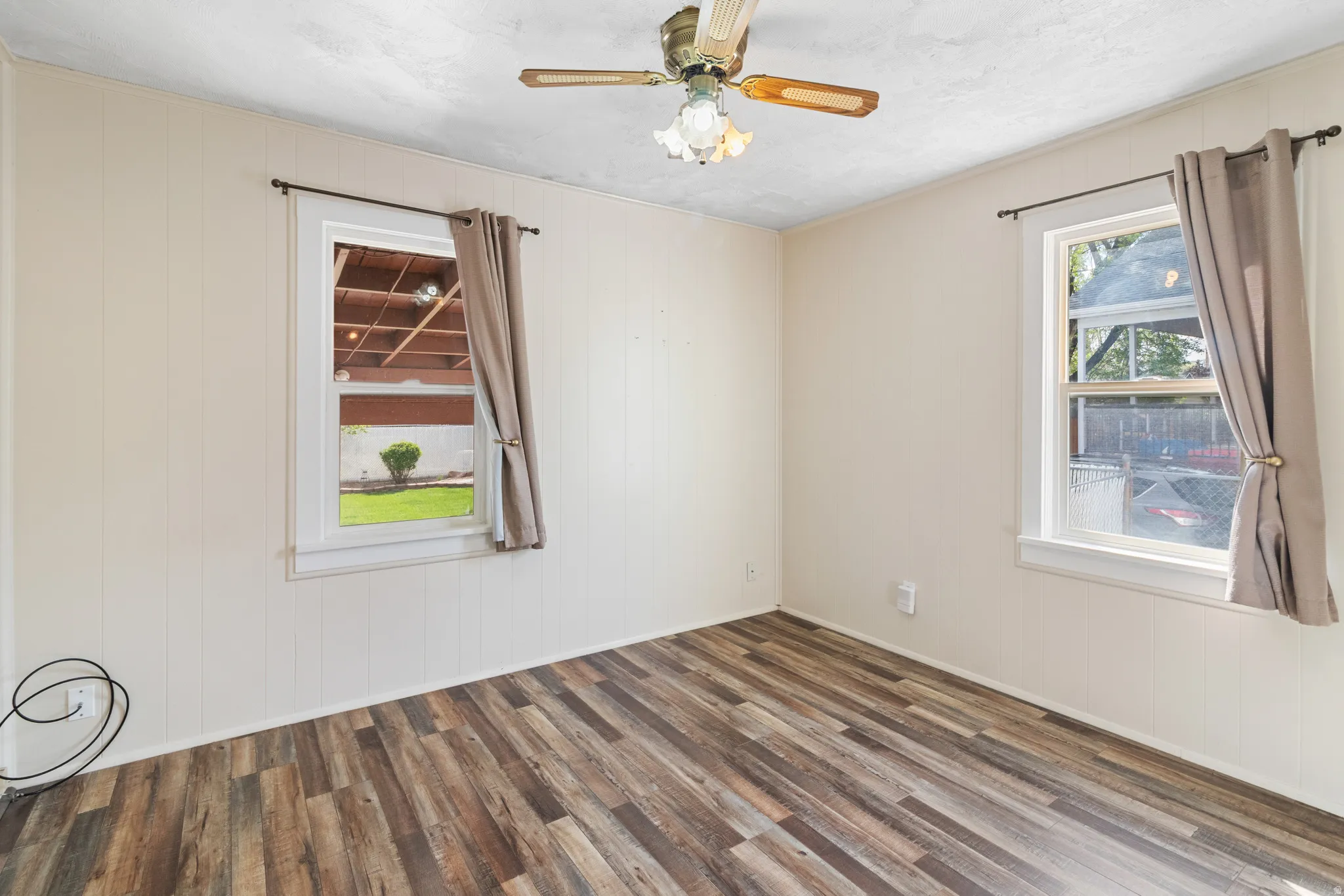 Empty room with dark wood-style floors, wood walls, and ceiling fan