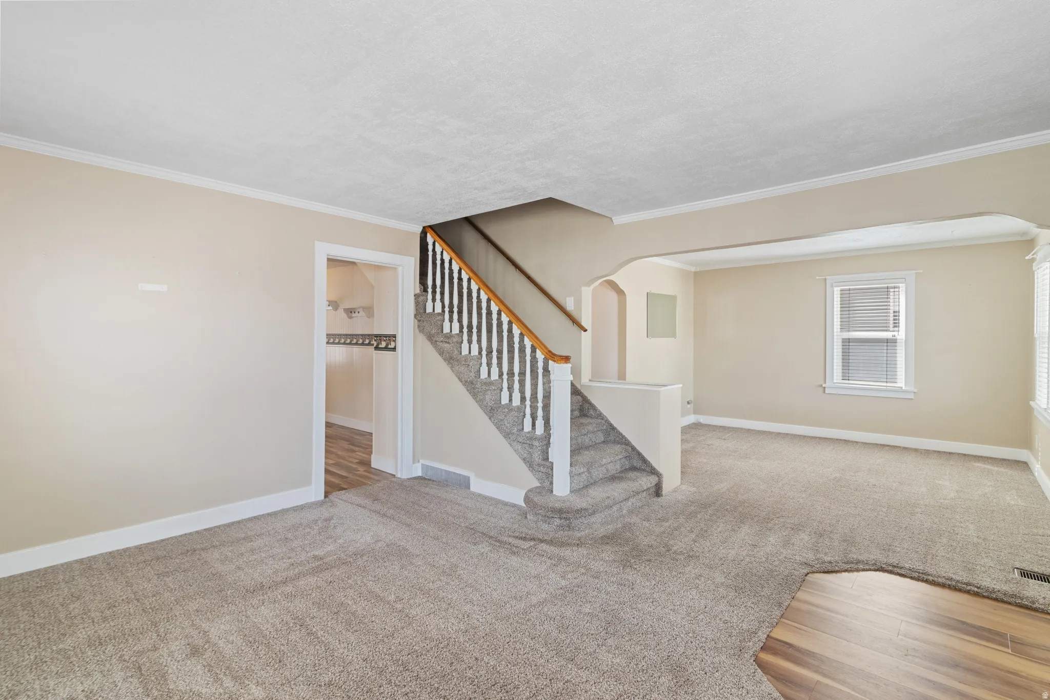 Unfurnished living room featuring arched walkways, light carpet, ornamental molding, a textured ceiling, and light wood-style flooring
