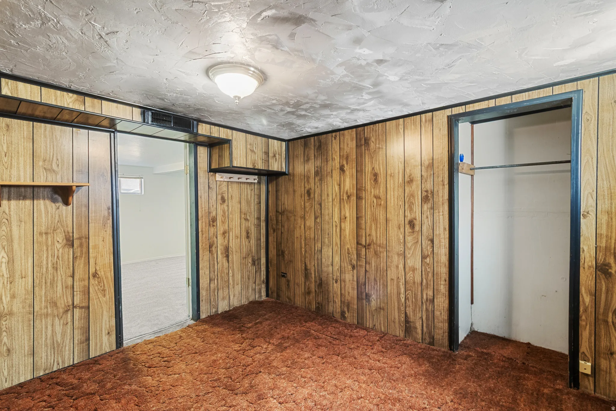 Unfurnished bedroom with dark colored carpet, wood walls, and a textured ceiling