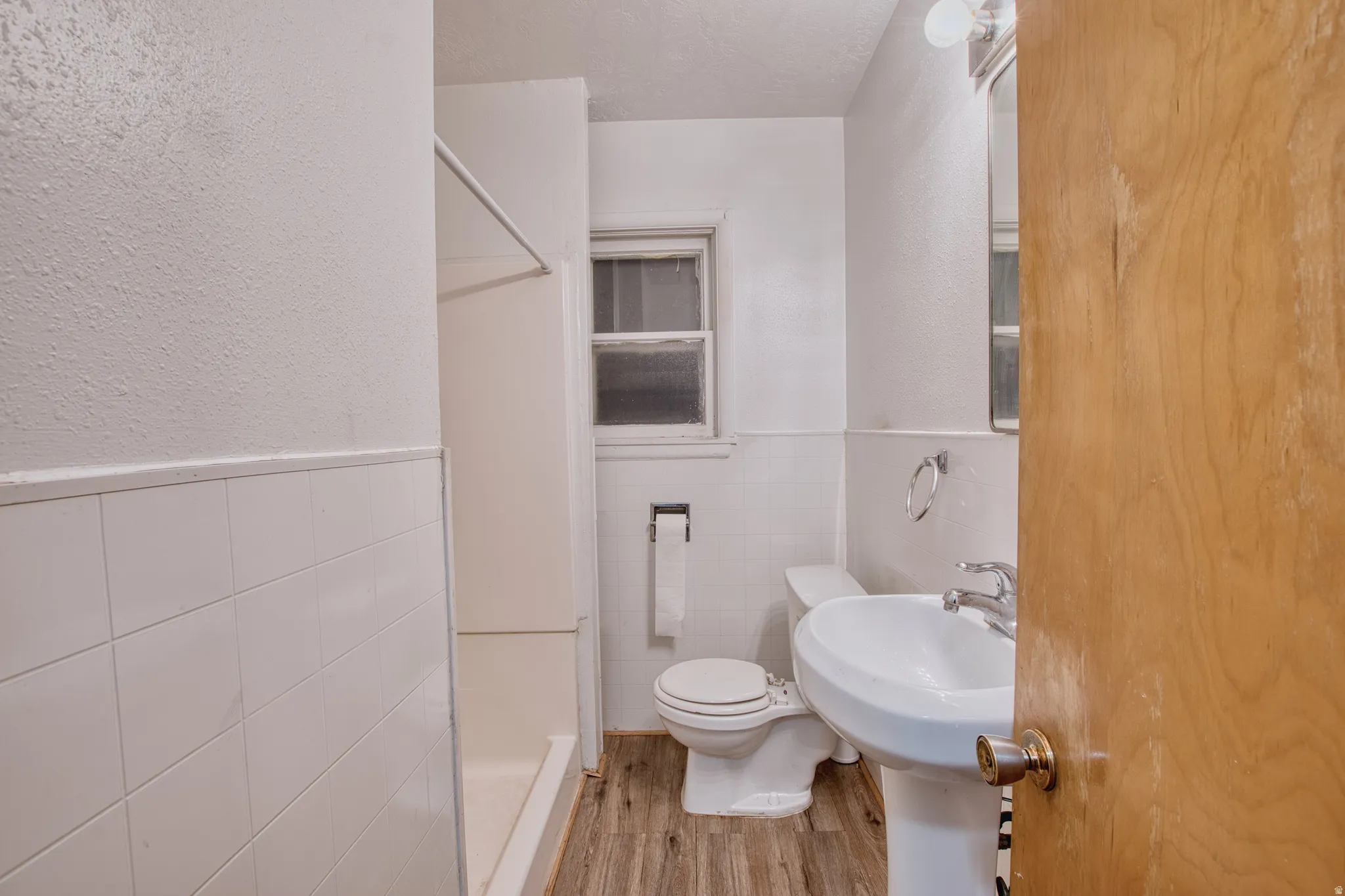 Full bathroom featuring a wainscoted wall, a stall shower, tile walls, light wood-type flooring, and a textured wall