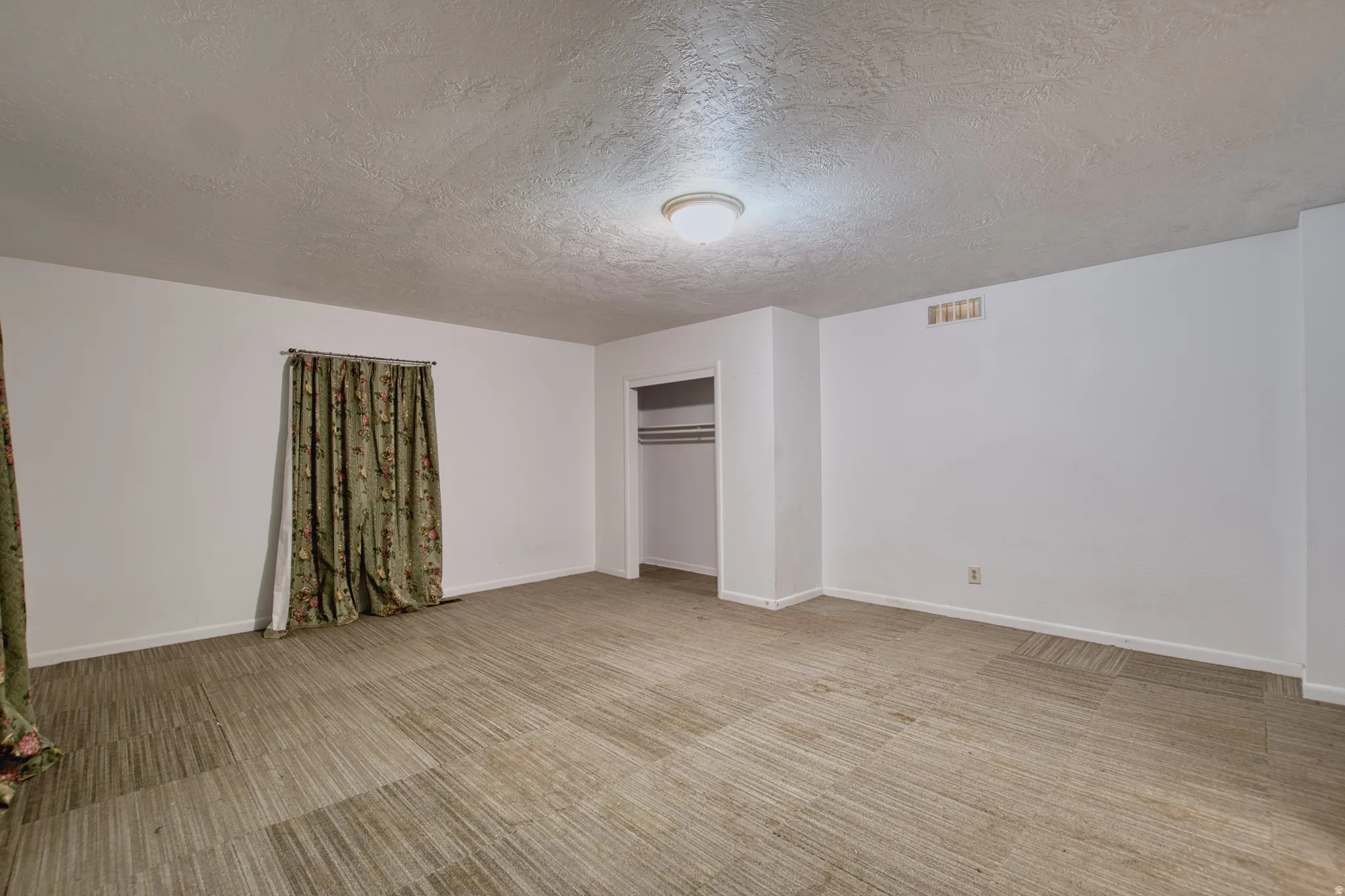 Unfurnished bedroom featuring light carpet, a textured ceiling, and a closet