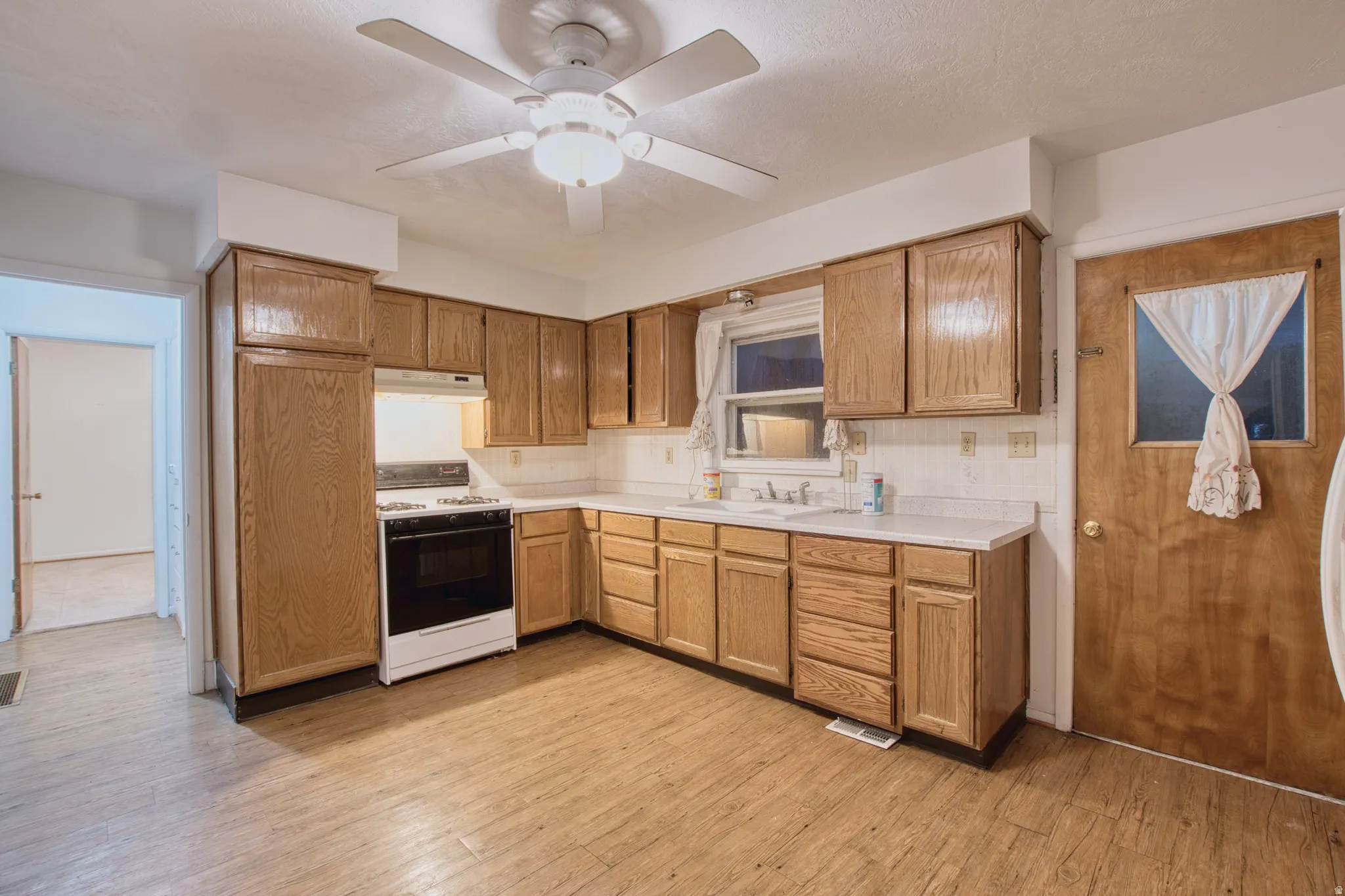 Kitchen featuring light countertops, white range with gas stovetop, ceiling fan, light wood-type flooring, and wood finish cabinets