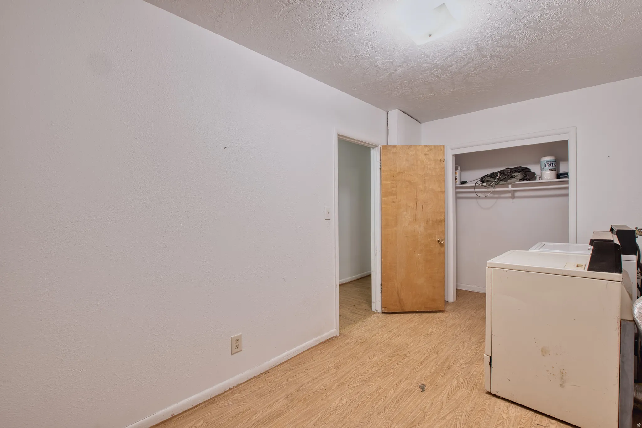 Laundry area featuring light wood-style floors, a textured ceiling, and independent washer and dryer