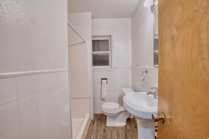 Full bathroom featuring a wainscoted wall, a stall shower, tile walls, light wood-type flooring, and a textured wall
