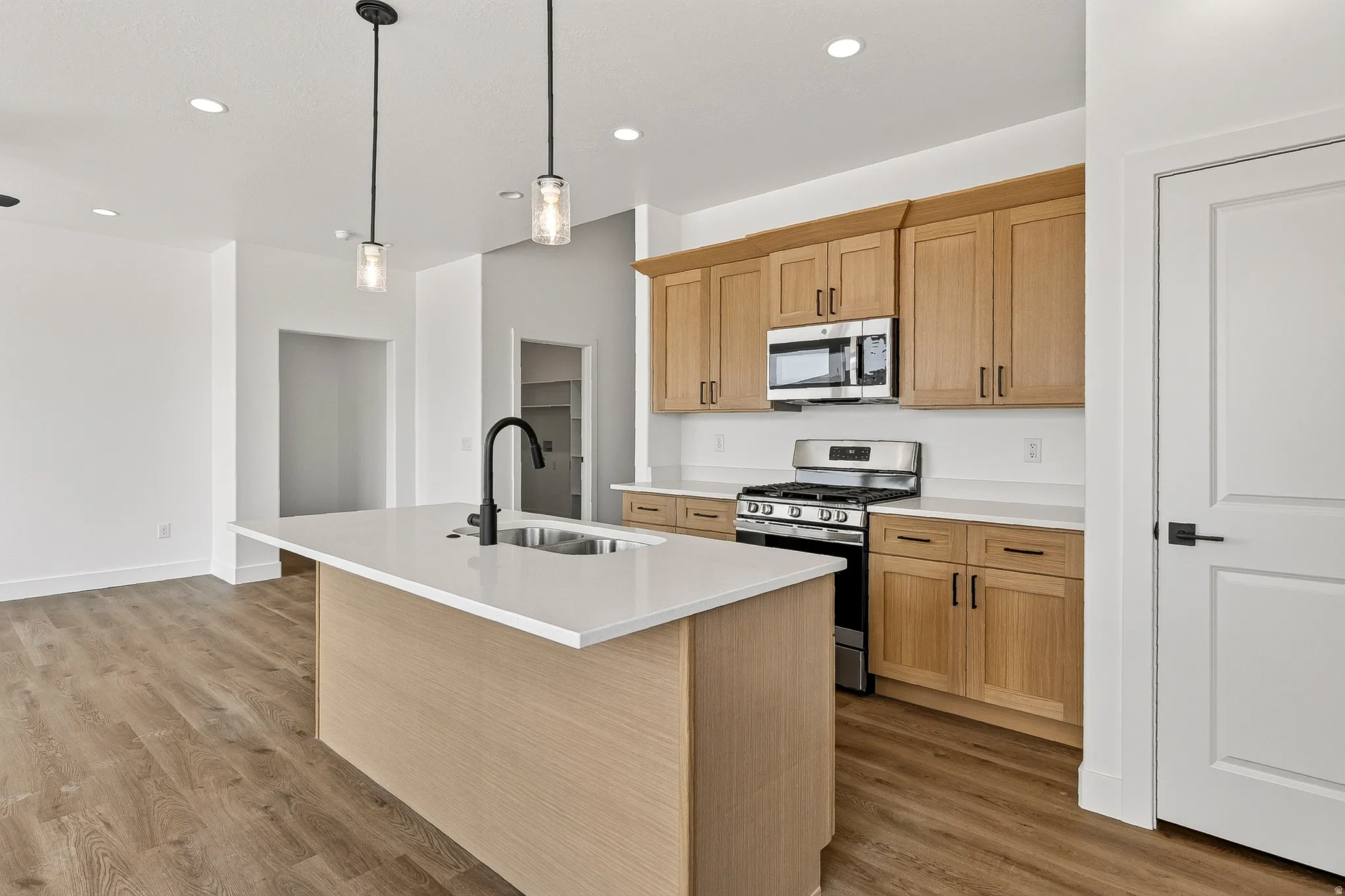 Kitchen featuring a central island with a sink, stainless steel appliances, light wood-finish cabinetry, and white countertops