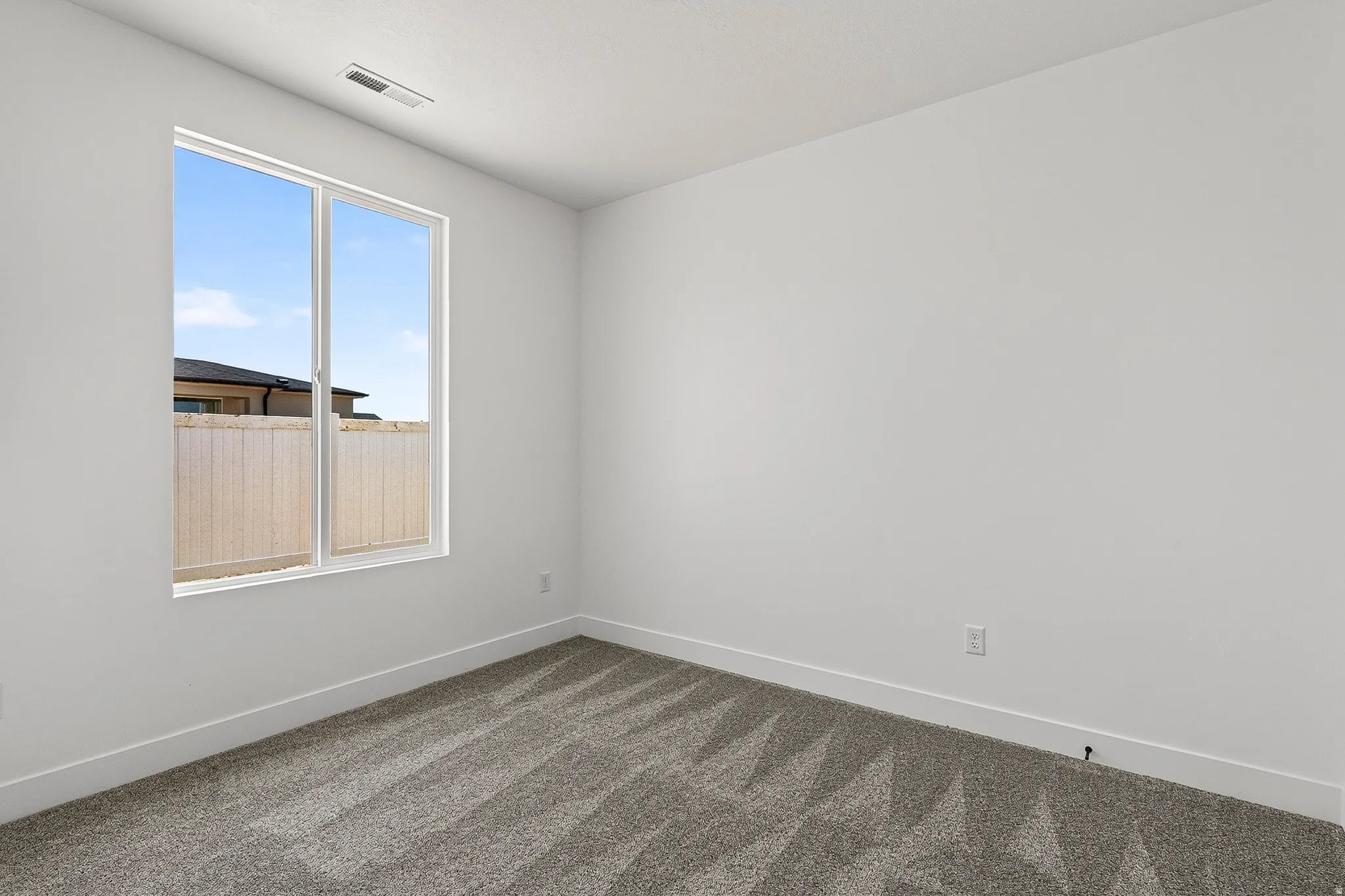 Room with a large window, gray patterned carpet, white baseboards, and white painted walls