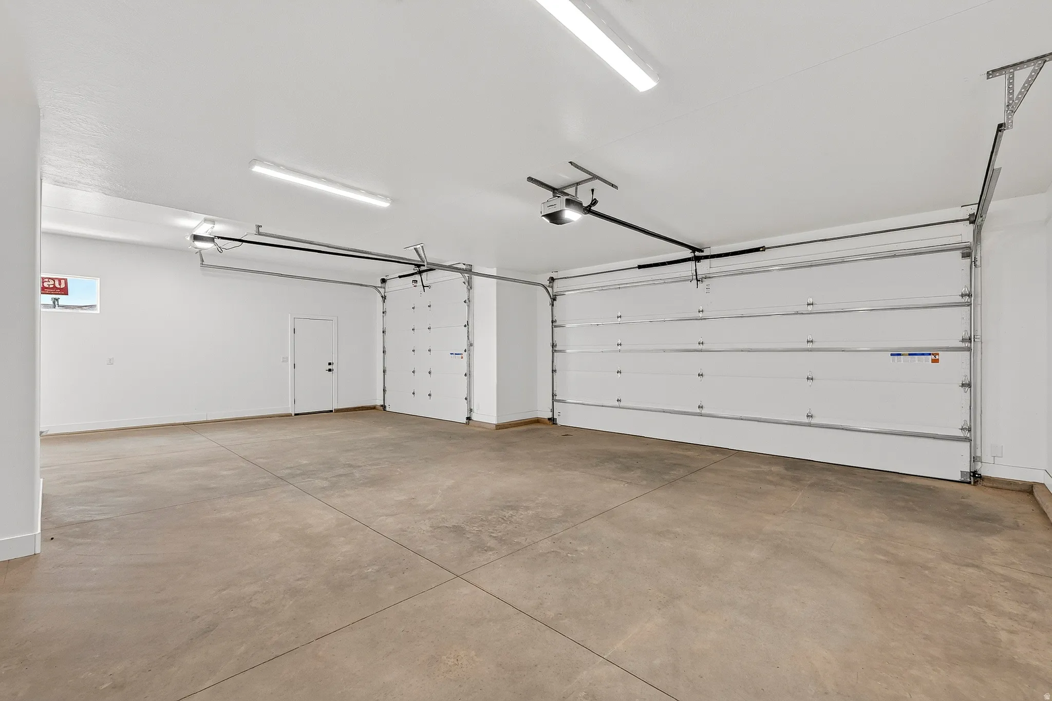 Spacious garage featuring two overhead doors with automatic openers, a pedestrian door, a small window, and concrete flooring