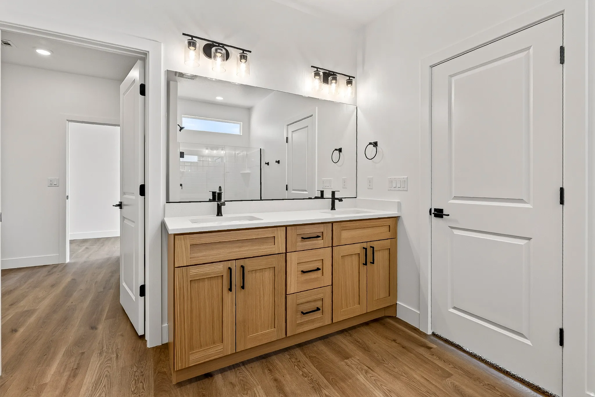 Double vanity featuring a light wood-finish cabinet with black hardware, white countertop, and dual vessel sinks with matte black faucets